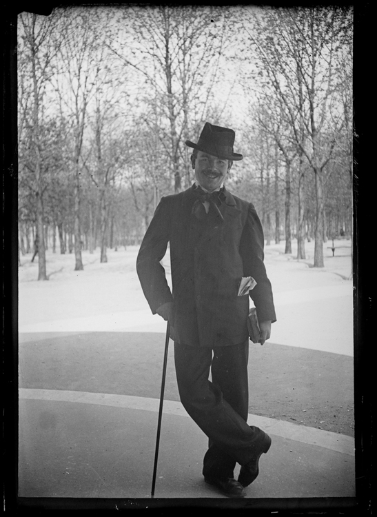 Un homme portant la moustache, en costume, s'appuyant sur sa canne