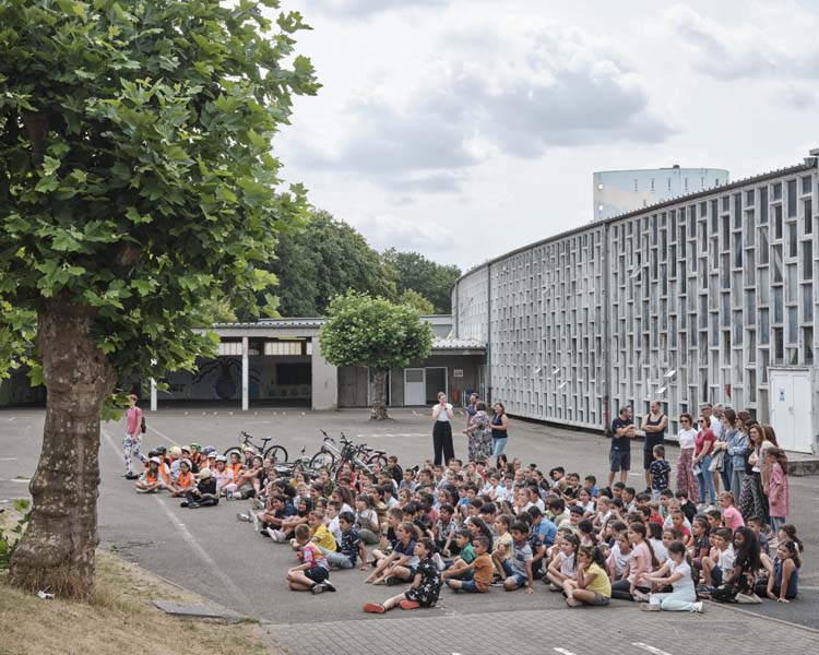 Rassemblements d’écoliers dans la cour de l’école ; A l’arrière-plan, préau et bâtiment vitré