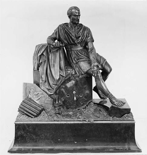 Pendule : personnage de l'Antiquité assis sur un bloc de pierre, au milieu de ruines, un parchemin à la main, bronze et ébène - © Ministère de la Culture (France), Médiathèque du patrimoine et de la photographie (objets mobiliers), tous droits réservés