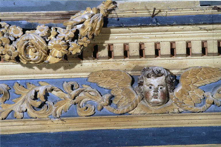 Retable : détail de la corniche sculptée d'une guirlande de fleurs, de rinceaux et d'un chérubin, bois sculpté, peint