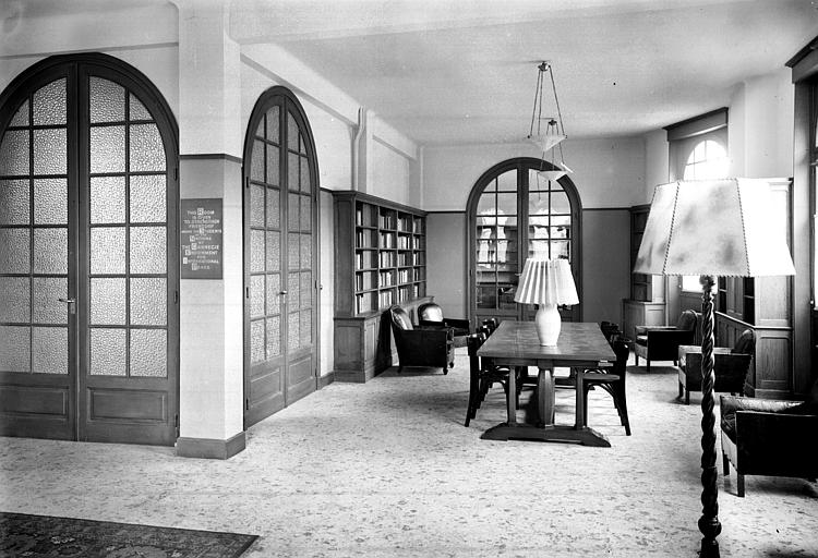 Intérieur, décoration de la bibliothèque : rayonnages, table, chaises, fauteuils, lampadaire, lampe