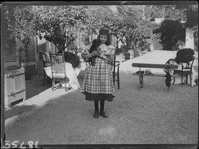 Jardin, petite fille posant avec un chien dans les bras, derrière femmes assises de dos