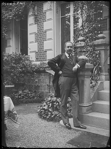 Portrait de Robert en civil, posant seul devant la façade d'une maison, accoudé au pilier de l'escalier