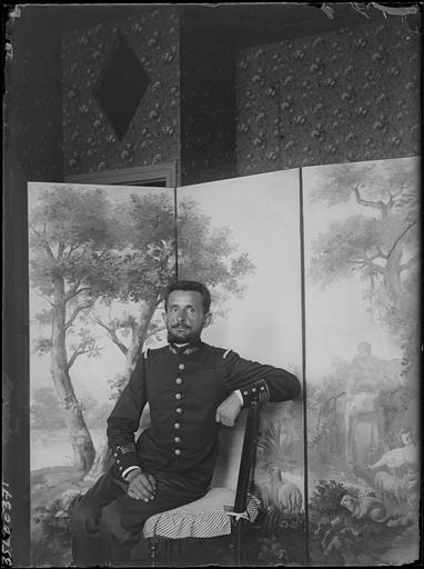 Intérieur : portrait du Commandant Marchand assis accoudé au dossier d'une chaise devant un paravent peint (scène bucolique)