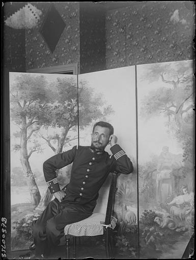 Intérieur : portrait du Commandant Marchand assis accoudé au dossier d'une chaise devant un paravent peint (scène bucolique), une main sur la hanche