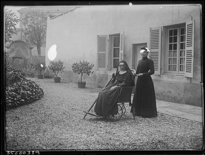 Jardin du cloître : religieuse en fauteuil roulant, jeune femme debout derrière elle
