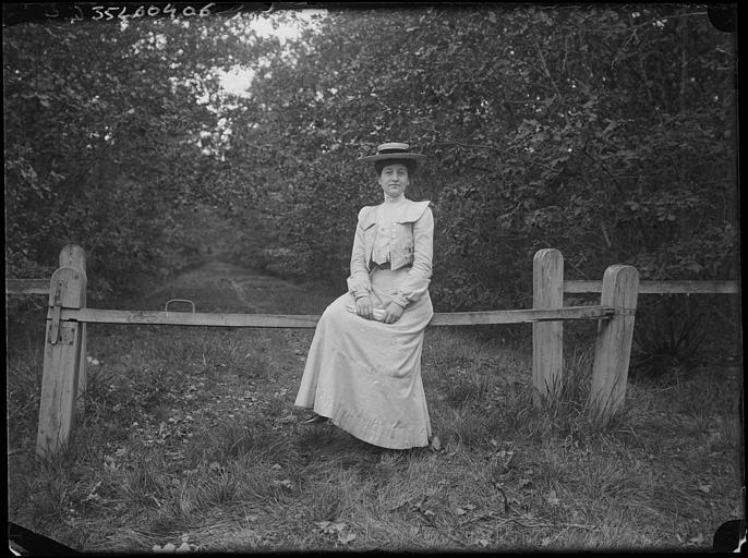 Allée forestière : portrait d'une femme assise sur une barrière en bois, de face
