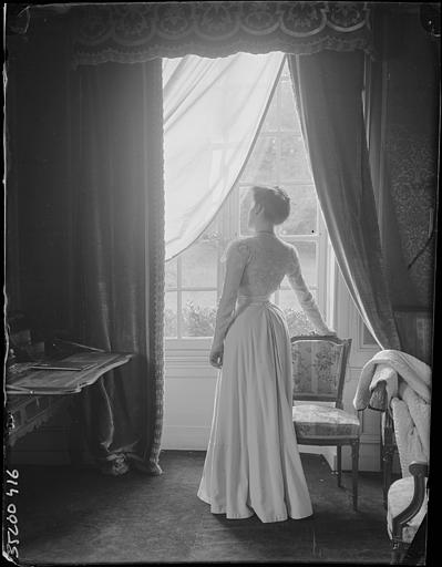 Intérieur : portrait d'une femme, de dos devant une fenêtre