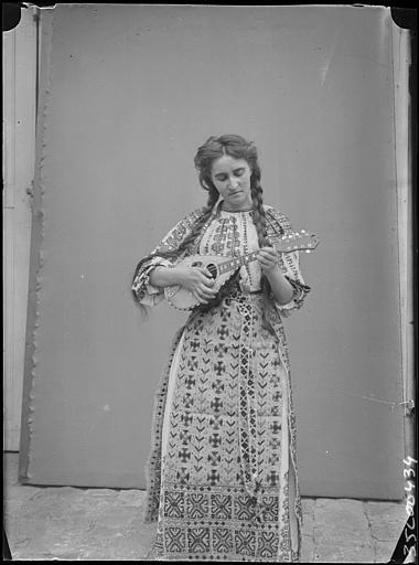 Extérieur, cour pavée, pose devant une toile : Mlle Desforges en roumaine avec une mandoline dans les mains, de face, visage penché