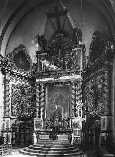 Retable architecturé à trois travées, surmonté d'un fronton agrémenté d'une Déploration du Christ en ronde-bosse, orné de deux statues de saints évêques, de trois toiles représentant de saints personnages, bois sculpté, peint, doré ; avant restauration