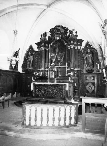 Autel sculpté de l'Agneau immolé et de motifs végétaux, surmonté de gradins et d'un tabernacle en forme de lanternon flanqué par deux statues d'anges adorateurs, retable architecturé à trois travées orné de deux statues d'évêques et d'un bas-relief représ