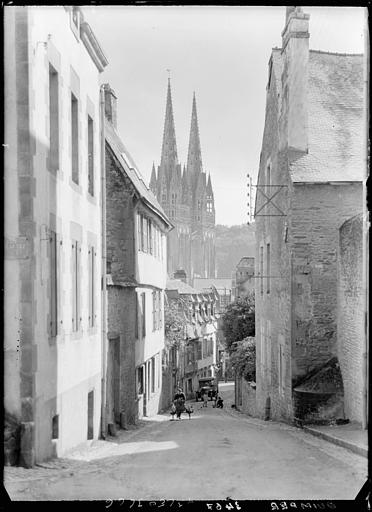 Une rue, les deux clochers et un breton avec une charette à bras