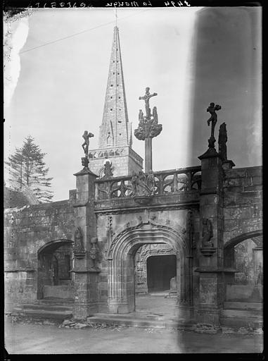 Calvaire au premier plan et portail de l'église à gauche