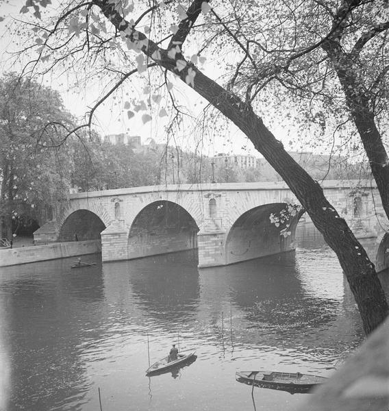 [Un homme pêche dans une barque, sur la Seine, à côté du Pont Marie]