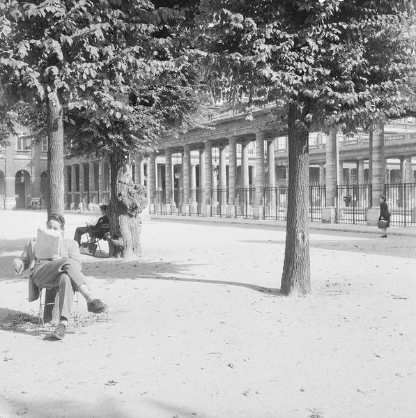 [Deux hommes en train de lire, assis contre des arbres du jardin du Palais-Royal]