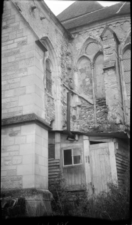 Angle du chevet et du transept ; fenêtres en partie murées ; cabane de planches dans l’angle