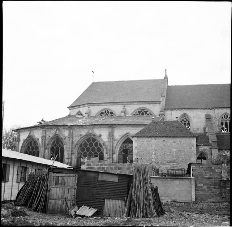 Chevet, façade latérale ; maison accolée et maisonnettes de bois jouxtant l’église