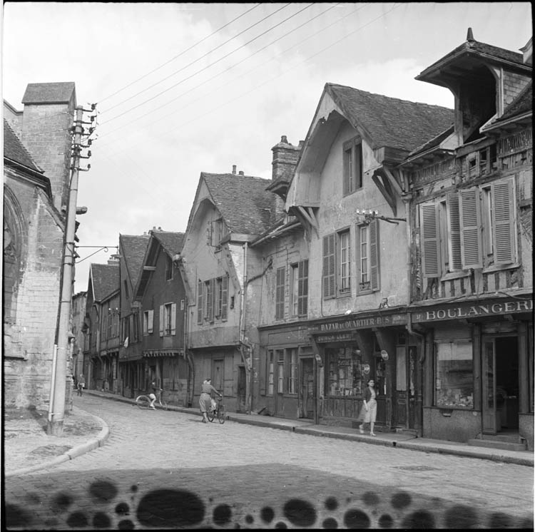 Abords ; alignement des façades sur la rue longeant l’église ; enseignes de boulangerie et de « Bazar de quartier »