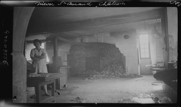 Intérieur, salle basse ou anciennes cuisines : four à bois (femme en pose croisant les bras)