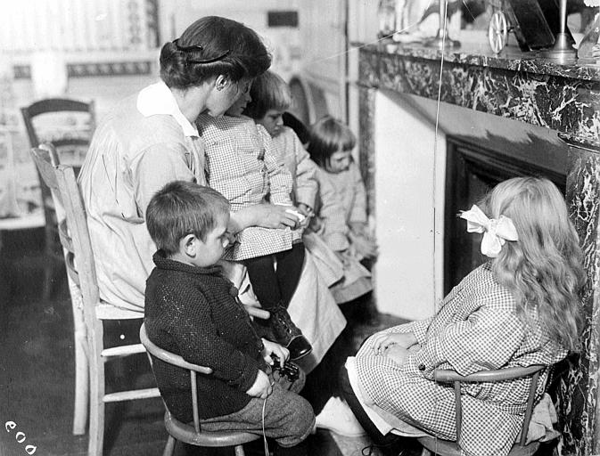 Intérieur, enfants avec une nurse devant une cheminée