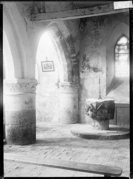 Intérieur : bas-côté avec colonnes à chapiteaux sculptés, vitrail et fonts baptismaux