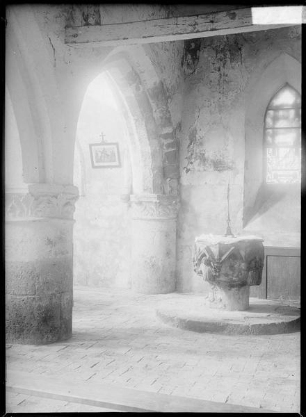 Intérieur : bas-côté avec colonnes à chapiteaux sculptés, vitrail et fonts baptismaux