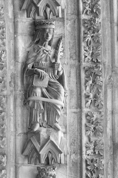 Portail central de la façade ouest, deuxième voussure droite, septième rangée : femme couronnée  assise tenant une palme et un livre, de trois quarts droit