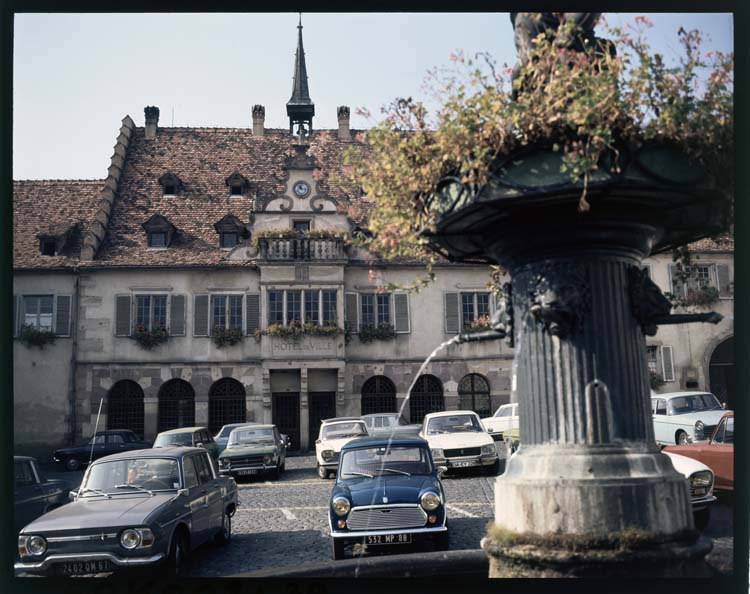 Façade est sur la place ; Fontaine ; Voitures stationnées