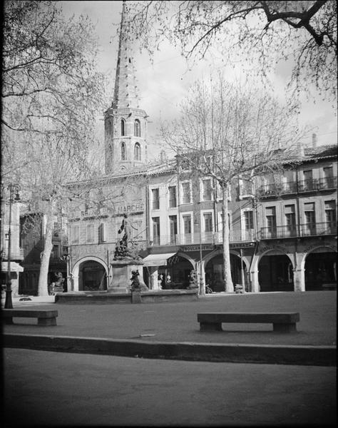 Façades à arcades sur place avec fontaine monumentale et clocher de l'église, côté ouest