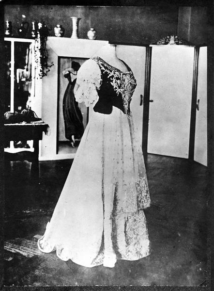 Costumes de couronnement des aristocrates austro-hongroises. Robe de la comtesse Hella von Hadik-Barkoczy. Robe avec petite traîne de soie blanche et broderie ancienne. Cette broderie se trouve aussi sur le « Pruszlik » (corsage) de satin noir et sur le tablier de tulle blanc. « Pruszlik » avec véritable rang de perles, et veste en brocard ancien à fleurs