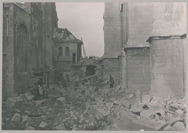 Entre les chevets de la cathédrale et de la chapelle archiépiscopale, détériorées par les bombardements ; Ouvrier cherchant des débris de sculptures dans les décombres