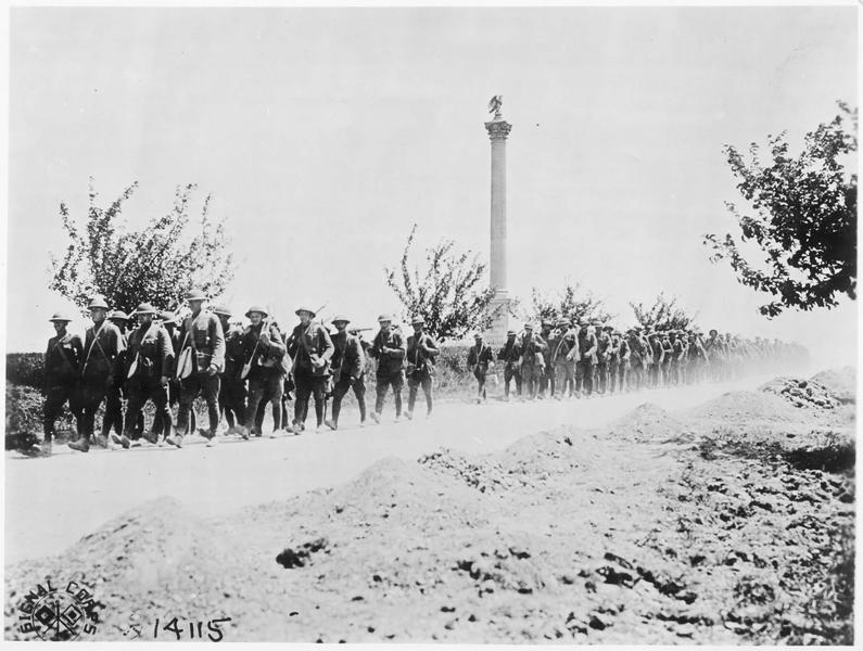 Soldats américains passant devant une colonne commémorative, placée au bord de la route