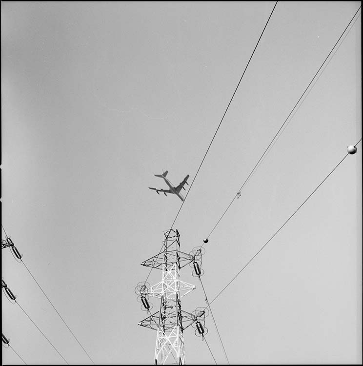 Avion survolant un pylône électrique quatre triangles