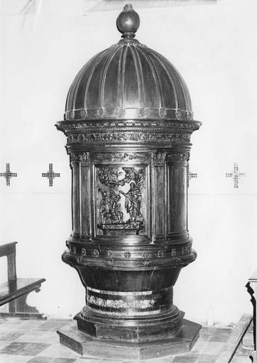 Fonts baptismaux fermés par un couvercle monumental évoquant la forme du tempietto de Bramante et sculpté en demi-relief de la scène du Baptême du Christ, bois sculpté