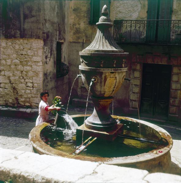 Une femme prenant de l'eau à la fontaine dans un seau