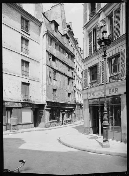 Maison à pans de bois ; devantures de l'Hôtel Volta, d'une épicerie-fruiterie, d'une blanchisserie, du Café « Chez Jean »