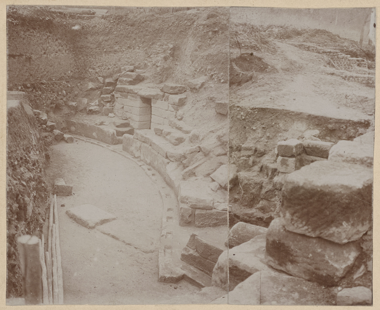 Partie sud-est du podium. Porte d’une cella. En avant, côté droit d’une des entrées latérales du postscenium. A gauche et au fond, terre restant à enlever et occupant le centre de l’arène. Cette vue est prise du chemin longeant le canal du Berry