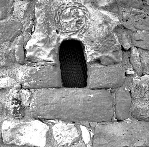 Croix gravée en pierre d'époque romane encastrée dans le mur du chevet