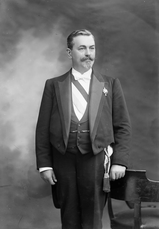 Camille Lenoir, homme politique. En mi-corps, debout, pose de trois quarts, appuyé sur le dossier d'un fauteuil.