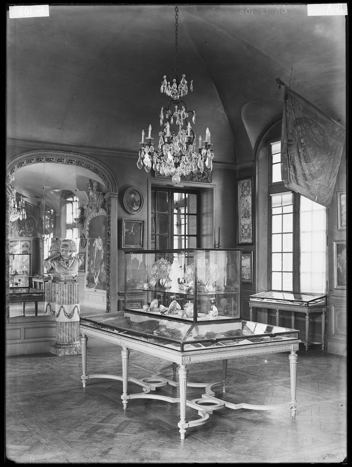 Salle d'exposition : grande vitrine centrale, lustre, buste en terre cuite, bannière