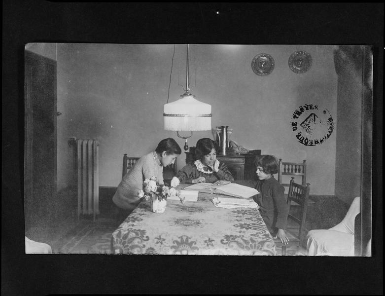 Portrait de Grazia Deledda et ses enfants Sardus et Franz regardant un album assis autour d'une table, dédicacé à Georges Hérelle