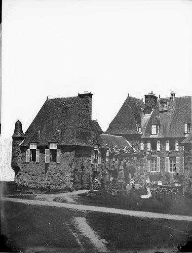 Vue de l'entrée, du pont-levis et des douves devant lesquelles se tiennent deux femmes en habit traditionnel normand