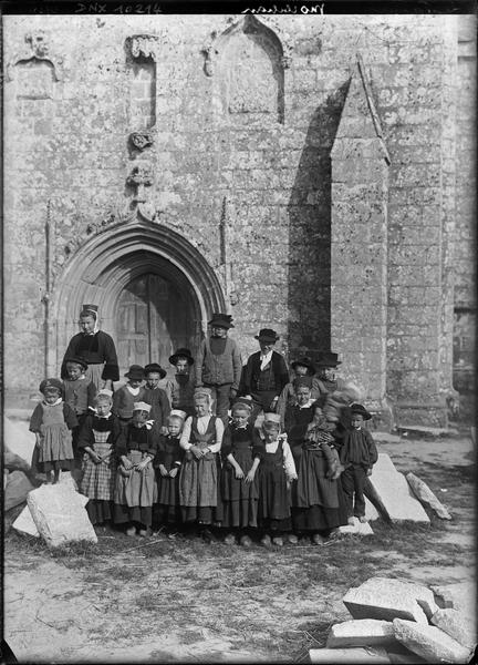 Portrait collectif : groupe de Bretons et Bretonnes en sabots et costume traditionnel devant le porche de la façade ouest