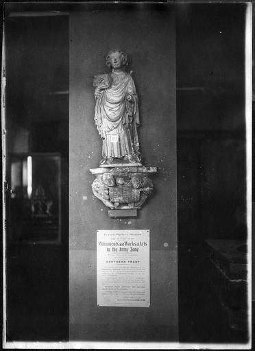 Statue : saint Quentin, en pierre, provenant de la collégiale de Saint-Quentin. Musée provisoire après l'occupation allemande. Affiche anglaise