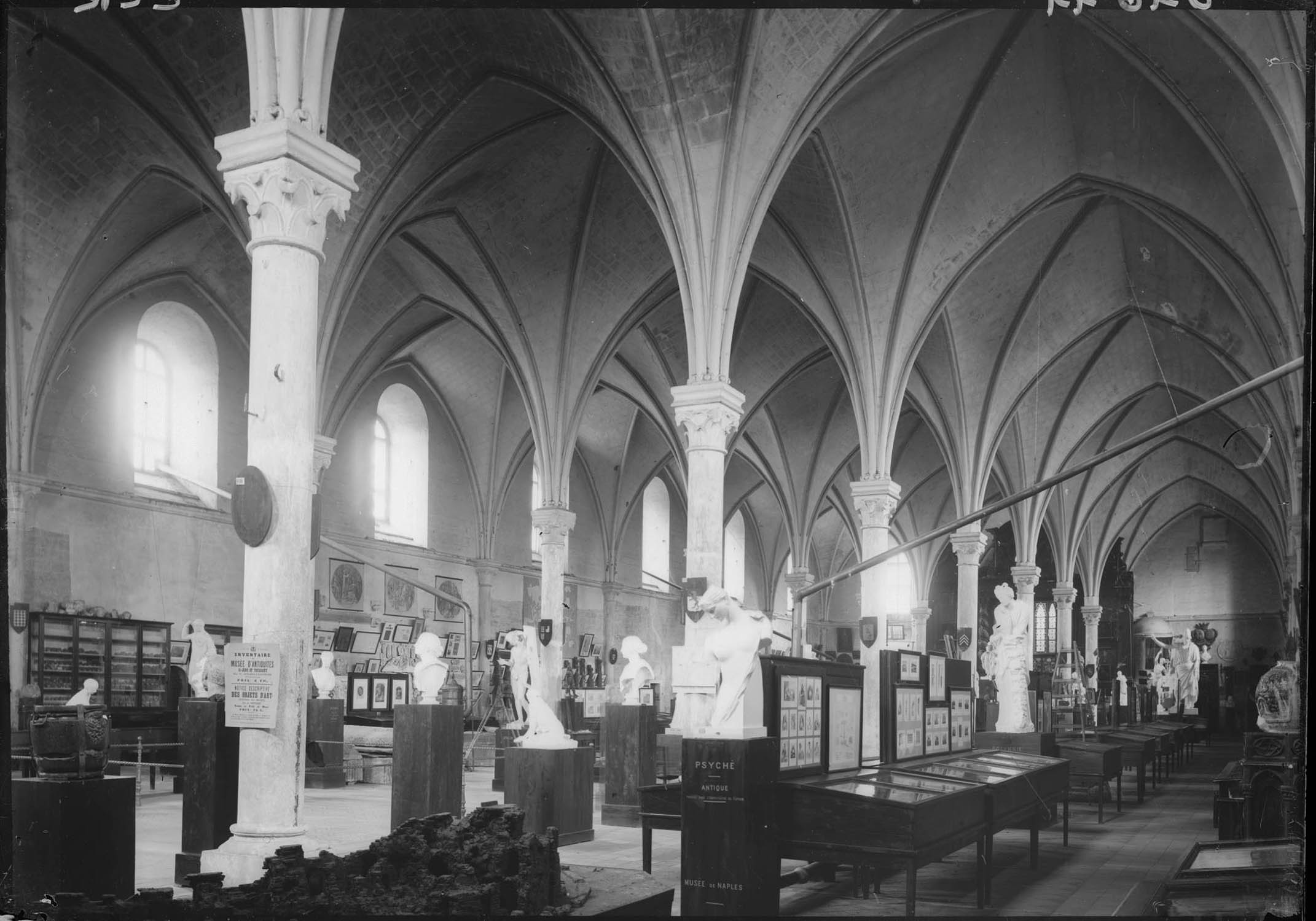 Vue intérieure de la salle Saint-Jean au temps du musée d’antiquités Saint-Jean-et-Toussaint : salle d'exposition, vitrines, statues