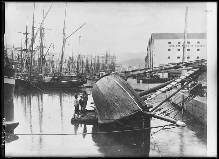 Vue sur le bassin, et les bateaux à voiles, un groupe examinant le fond du bateau couché sur le flanc à quai