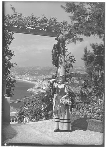 Femme en costume régional posant près d'une pergola. Vue sur le port