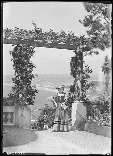 Femme en costume régional posant près d'une pergola. Vue sur le port