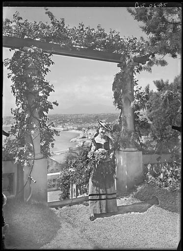 Femme en costume régional posant près d'une pergola. Vue sur le port