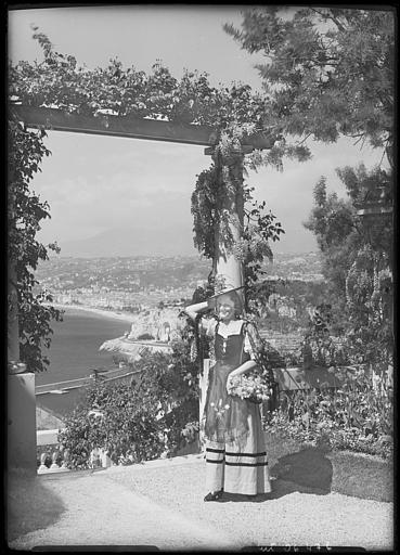 Femme en costume régional posant près d'une pergola. Vue sur le port